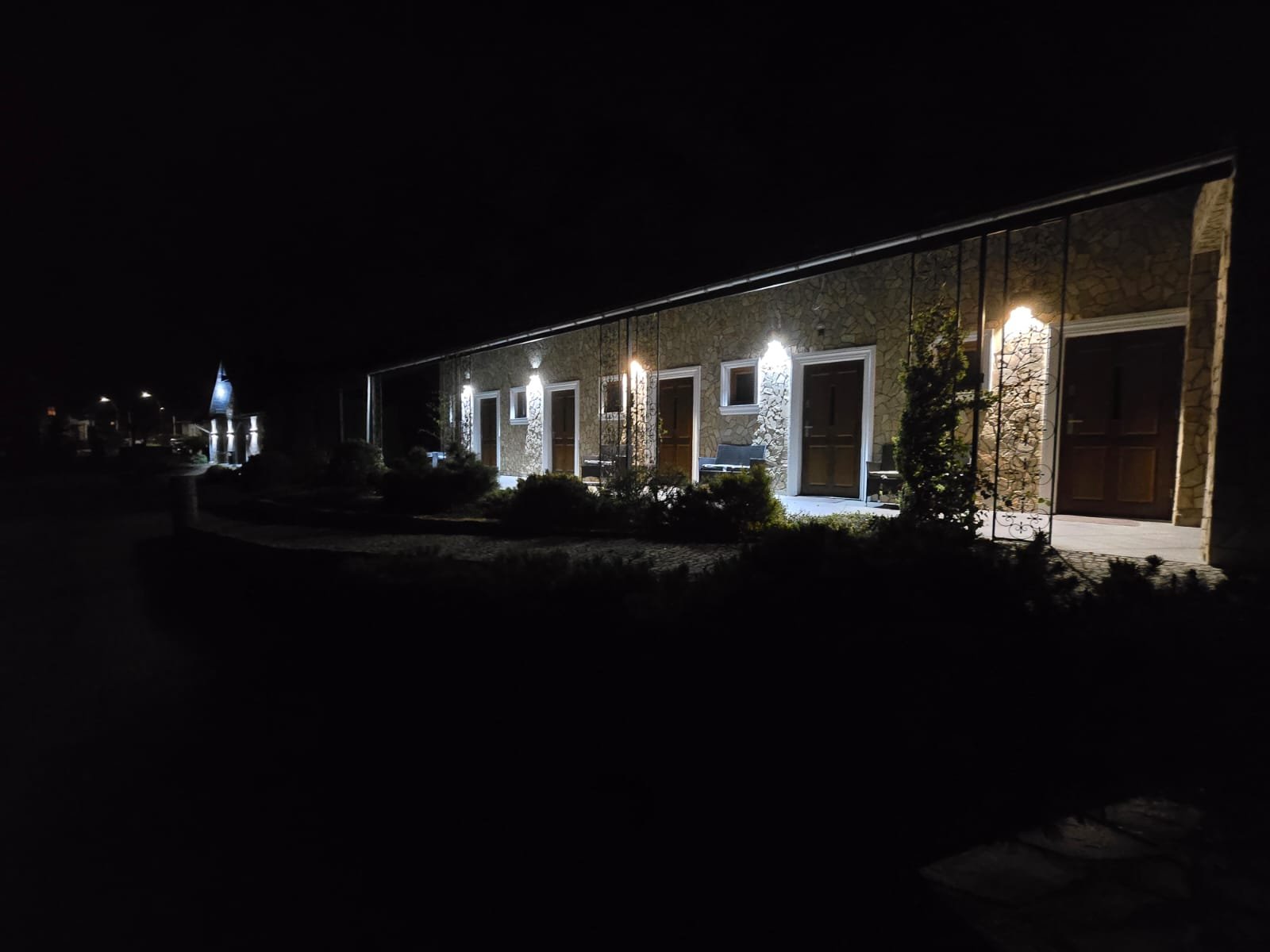 Kamienny dworek nocą — oświetlone kinkiety, osobne drzwi do pokoi